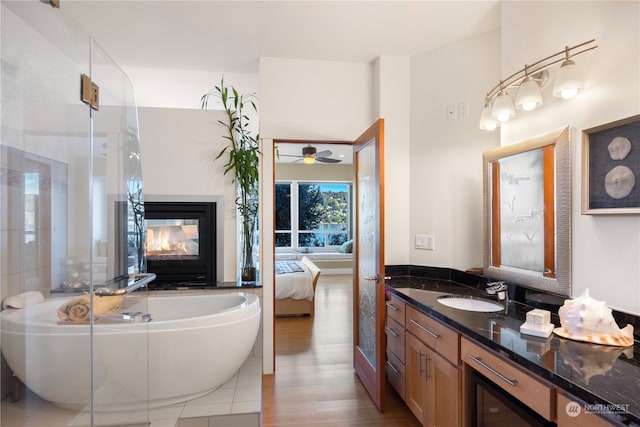 bathroom featuring vanity, a multi sided fireplace, hardwood / wood-style flooring, ceiling fan, and a washtub