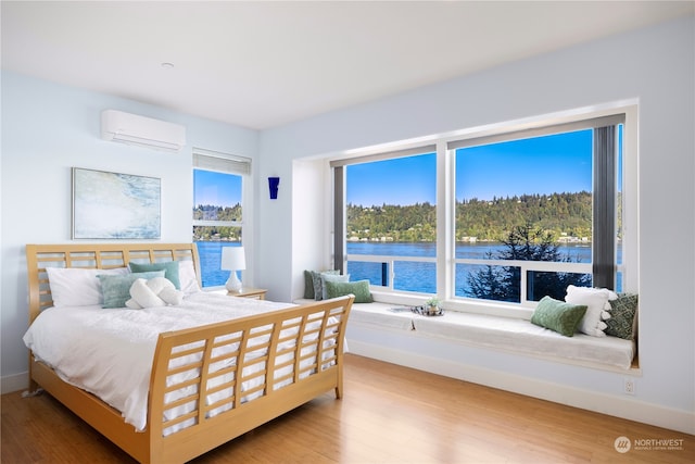 bedroom featuring an AC wall unit, hardwood / wood-style floors, and a water view