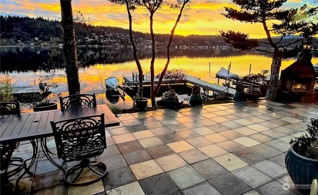 patio terrace at dusk featuring a water view and a dock