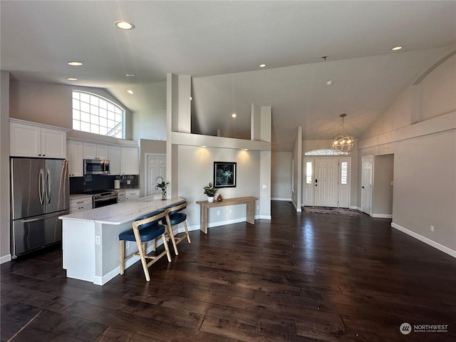 kitchen featuring a kitchen bar, light stone counters, hanging light fixtures, stainless steel appliances, and white cabinets