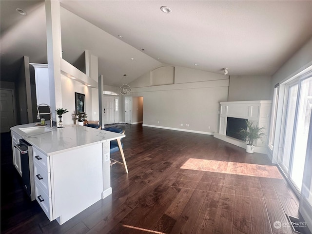 kitchen featuring sink, white cabinetry, dark hardwood / wood-style floors, light stone counters, and a center island with sink