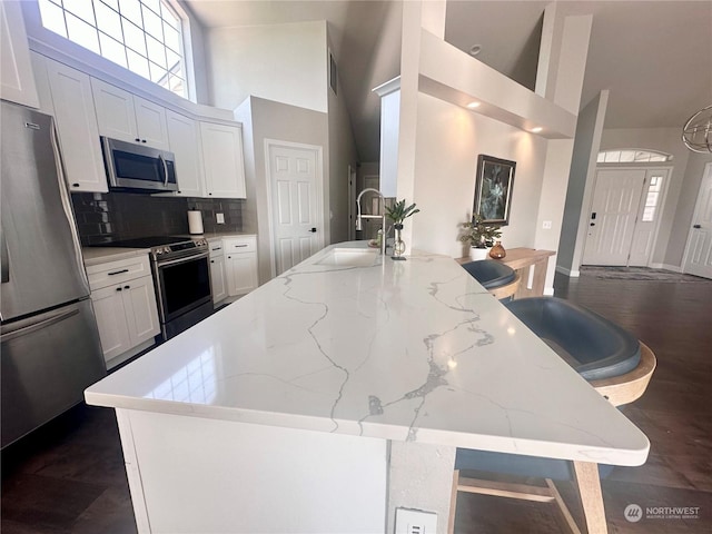 kitchen with sink, white cabinetry, stainless steel appliances, a kitchen breakfast bar, and light stone countertops