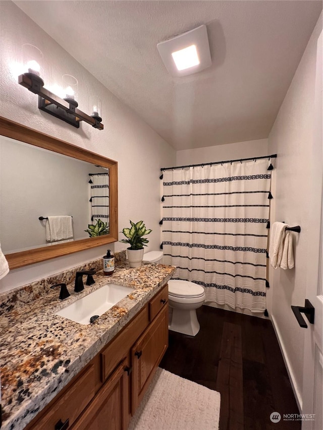 bathroom with toilet, a textured ceiling, vanity, curtained shower, and hardwood / wood-style flooring