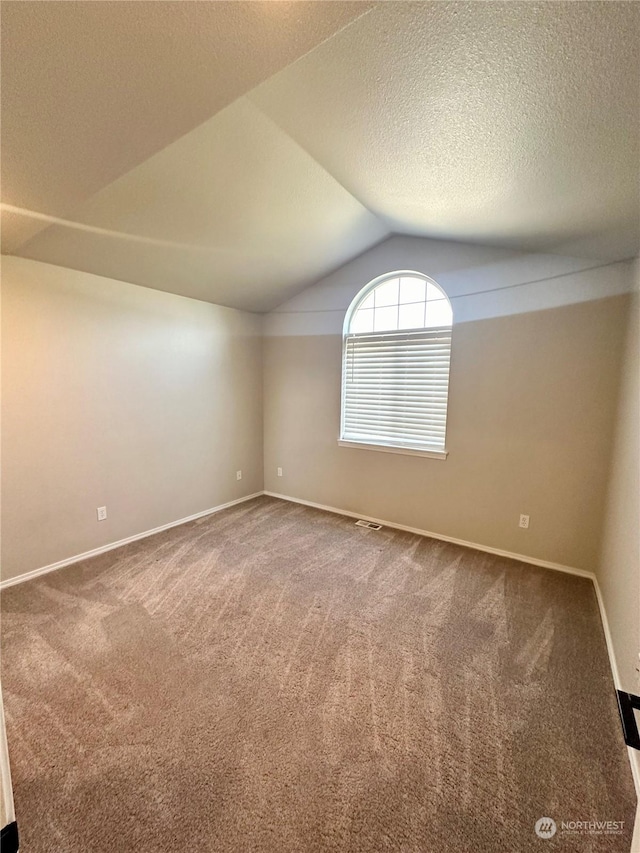 carpeted empty room featuring vaulted ceiling and a textured ceiling