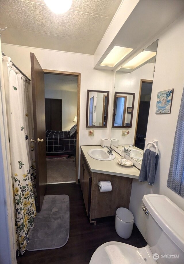 bathroom with a textured ceiling, vanity, curtained shower, hardwood / wood-style floors, and toilet