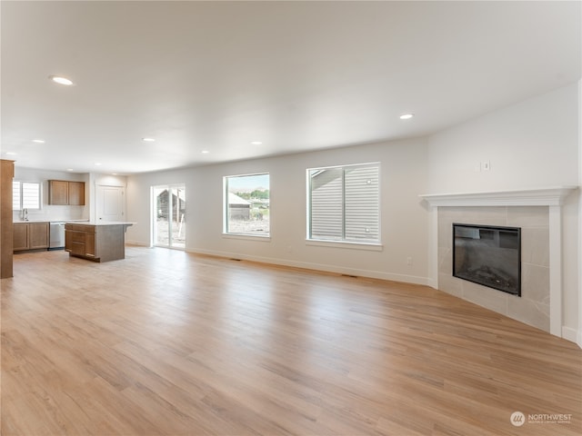 unfurnished living room featuring sink, a tiled fireplace, and light hardwood / wood-style floors