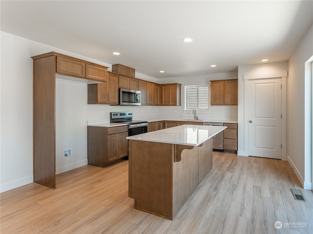 kitchen featuring a kitchen island, a kitchen breakfast bar, sink, appliances with stainless steel finishes, and light hardwood / wood-style floors