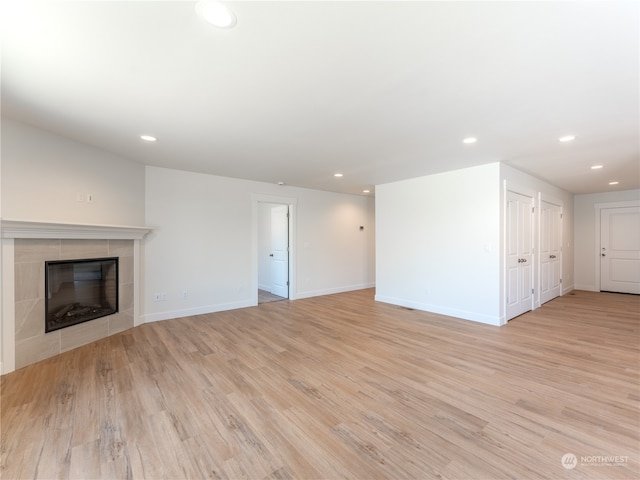 unfurnished living room with a tiled fireplace and light wood-type flooring