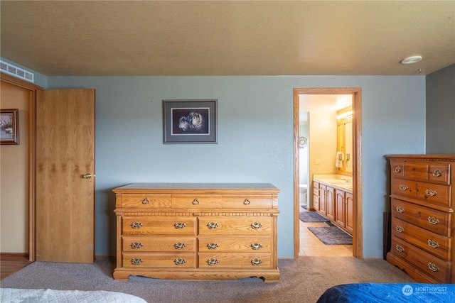 bedroom featuring connected bathroom, visible vents, a sink, and light colored carpet