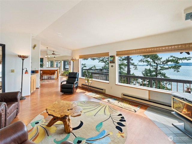 living area with light wood-style flooring, a baseboard radiator, a water view, and lofted ceiling