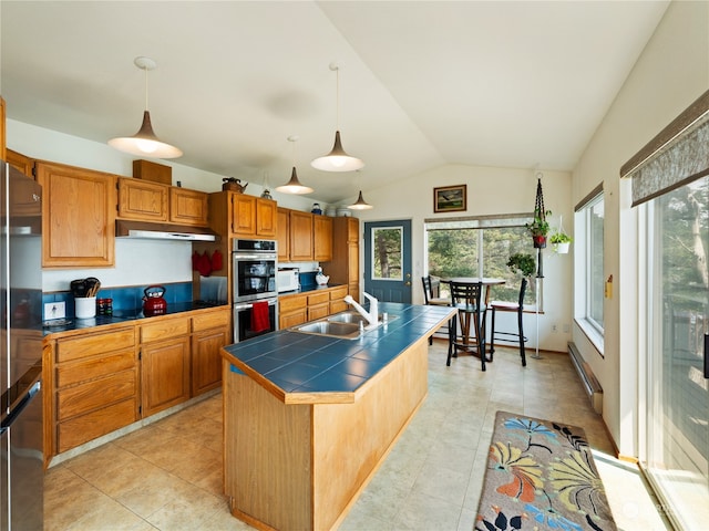 kitchen featuring double oven, light tile patterned floors, decorative light fixtures, an island with sink, and sink