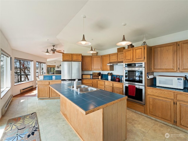 kitchen with stainless steel appliances, tile counters, a kitchen island with sink, and a sink