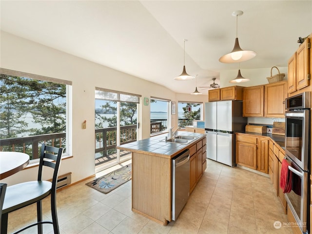 kitchen with tile countertops, vaulted ceiling, appliances with stainless steel finishes, baseboard heating, and decorative light fixtures