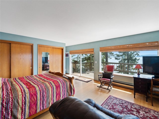 bedroom with multiple closets, access to exterior, baseboard heating, and light wood-style floors