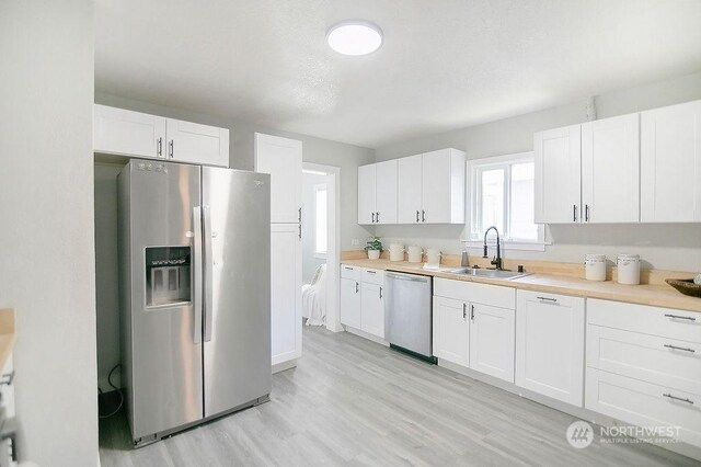 kitchen with white cabinetry, sink, stainless steel appliances, and light wood-type flooring