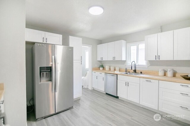 317 2nd Ave NW, Kelso, WA 98626 - kitchen featuring a sink, white cabinetry, stainless steel appliances, light wood-style floors, and light countertops
