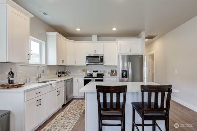 kitchen with white cabinetry, sink, wood-type flooring, a kitchen island, and appliances with stainless steel finishes