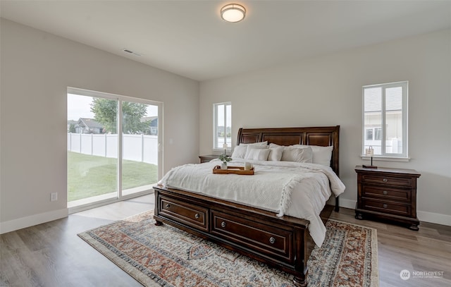 bedroom with access to outside, multiple windows, and light wood-type flooring