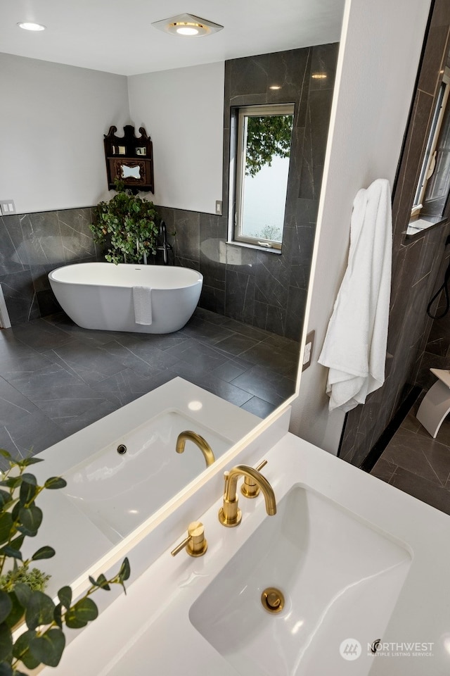 bathroom with a washtub, tile walls, sink, and tile patterned flooring