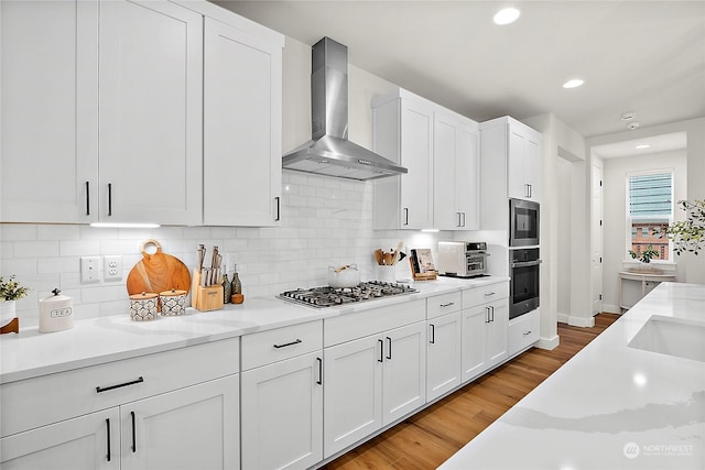 kitchen featuring white cabinets, stainless steel appliances, wall chimney exhaust hood, and light stone counters