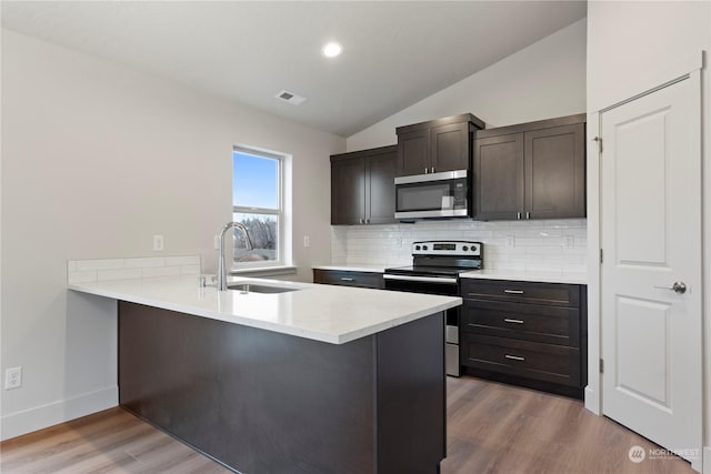 kitchen with kitchen peninsula, sink, lofted ceiling, and appliances with stainless steel finishes