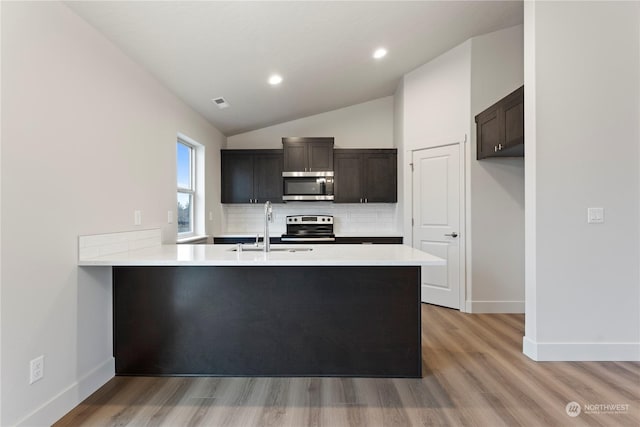 kitchen with kitchen peninsula, dark brown cabinets, stainless steel appliances, and vaulted ceiling