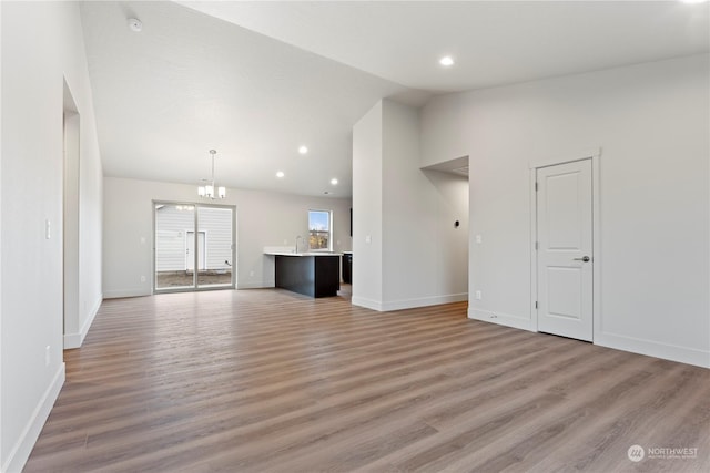 unfurnished living room featuring a notable chandelier, sink, vaulted ceiling, and hardwood / wood-style flooring