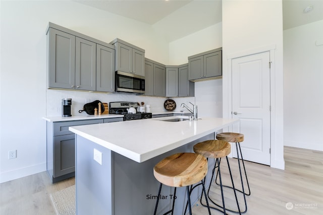 kitchen with sink, gray cabinetry, a kitchen bar, stainless steel appliances, and a center island with sink