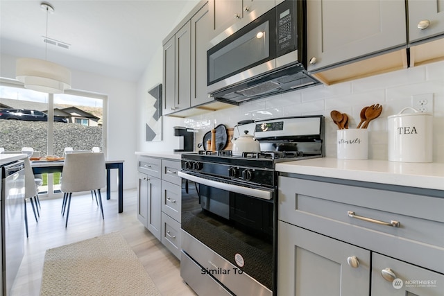 kitchen featuring gray cabinetry, tasteful backsplash, vaulted ceiling, light wood-type flooring, and stainless steel appliances