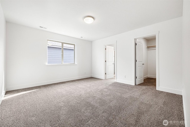 unfurnished bedroom featuring carpet floors, a walk in closet, visible vents, and baseboards