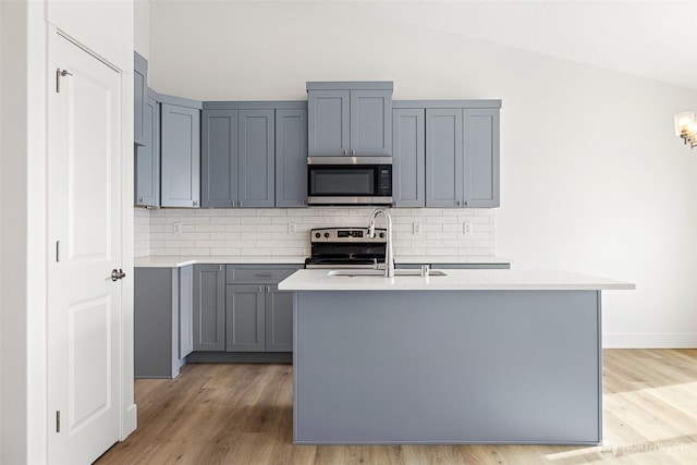 kitchen with vaulted ceiling, gray cabinets, stainless steel appliances, light countertops, and a sink