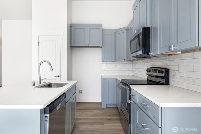 kitchen with a sink, light countertops, appliances with stainless steel finishes, light wood finished floors, and tasteful backsplash