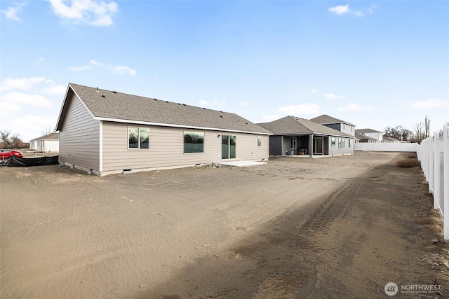 rear view of house featuring a shingled roof and fence