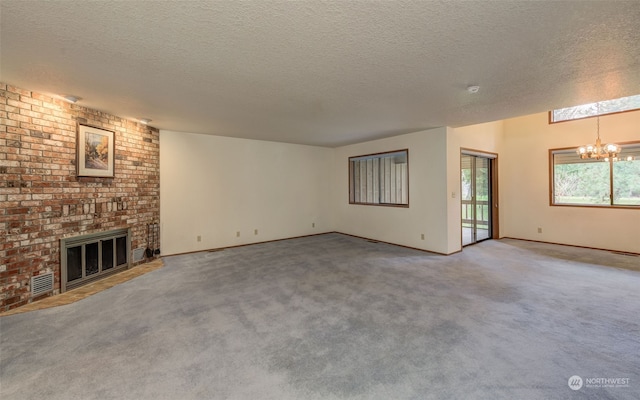 unfurnished living room featuring a textured ceiling, a chandelier, brick wall, a fireplace, and carpet