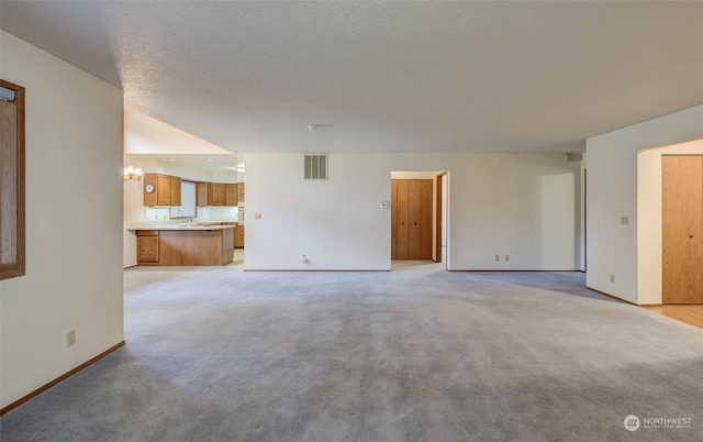 unfurnished living room featuring a textured ceiling, a chandelier, and light carpet