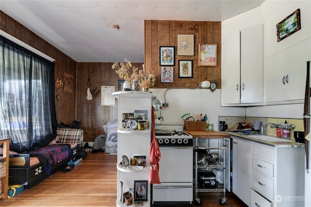 kitchen featuring wooden walls, light wood-type flooring, gas range gas stove, and white cabinetry