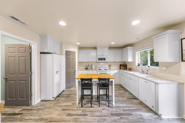 kitchen featuring a kitchen bar, white cabinets, a kitchen island, white appliances, and sink