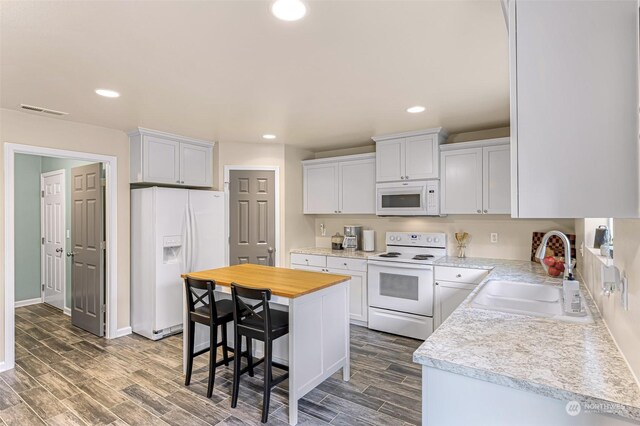 kitchen featuring white cabinetry, sink, a kitchen island, white appliances, and a breakfast bar area