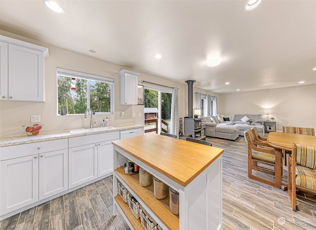 kitchen with wooden counters, light wood-type flooring, sink, white cabinetry, and a wood stove