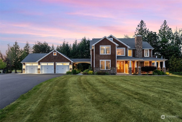 view of front facade featuring a porch, a garage, driveway, a front lawn, and a chimney