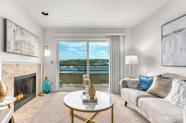 living room featuring a tiled fireplace, a water view, and light colored carpet