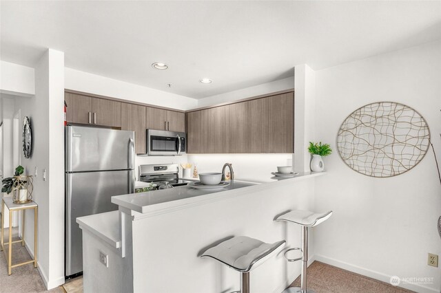 kitchen with appliances with stainless steel finishes, kitchen peninsula, light carpet, and sink