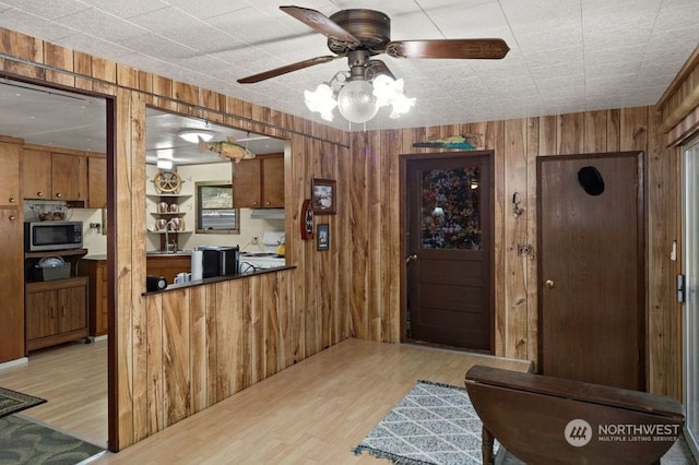 kitchen with light hardwood / wood-style flooring, range, wooden walls, ceiling fan, and kitchen peninsula