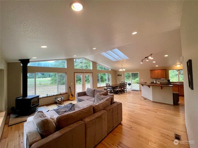 living room featuring vaulted ceiling with skylight, light hardwood / wood-style flooring, a wood stove, and a textured ceiling