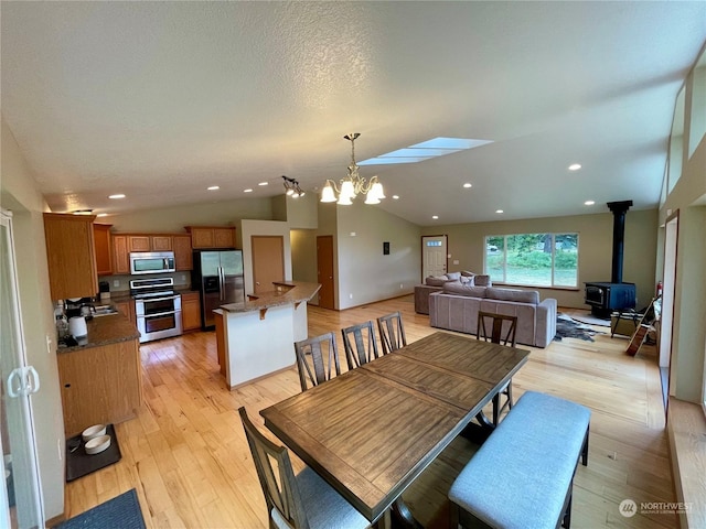 dining space featuring lofted ceiling, a chandelier, recessed lighting, light wood-type flooring, and a wood stove