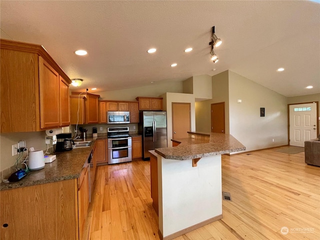 kitchen with light wood-style flooring, a breakfast bar, vaulted ceiling, appliances with stainless steel finishes, and brown cabinetry