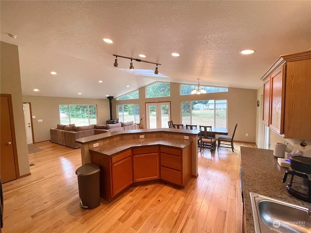 kitchen featuring lofted ceiling, open floor plan, a wood stove, and light wood-style floors