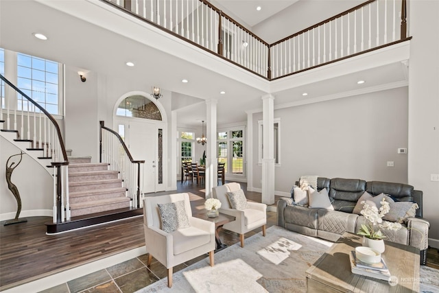 living room with a notable chandelier, a high ceiling, ornate columns, hardwood / wood-style floors, and crown molding