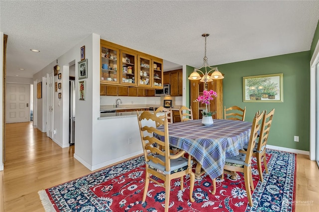 dining space featuring an inviting chandelier, sink, a textured ceiling, and light wood-type flooring