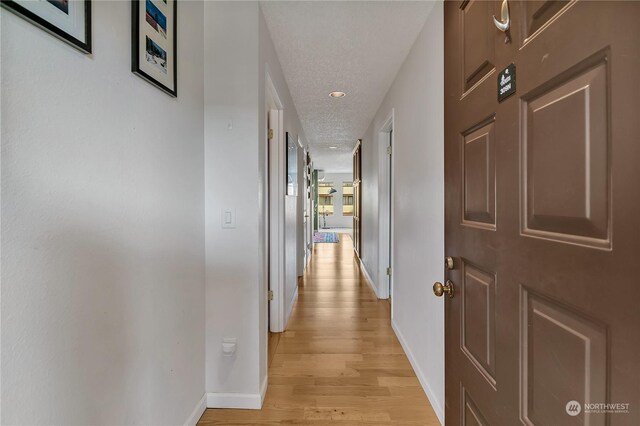 corridor featuring a textured ceiling and light hardwood / wood-style flooring